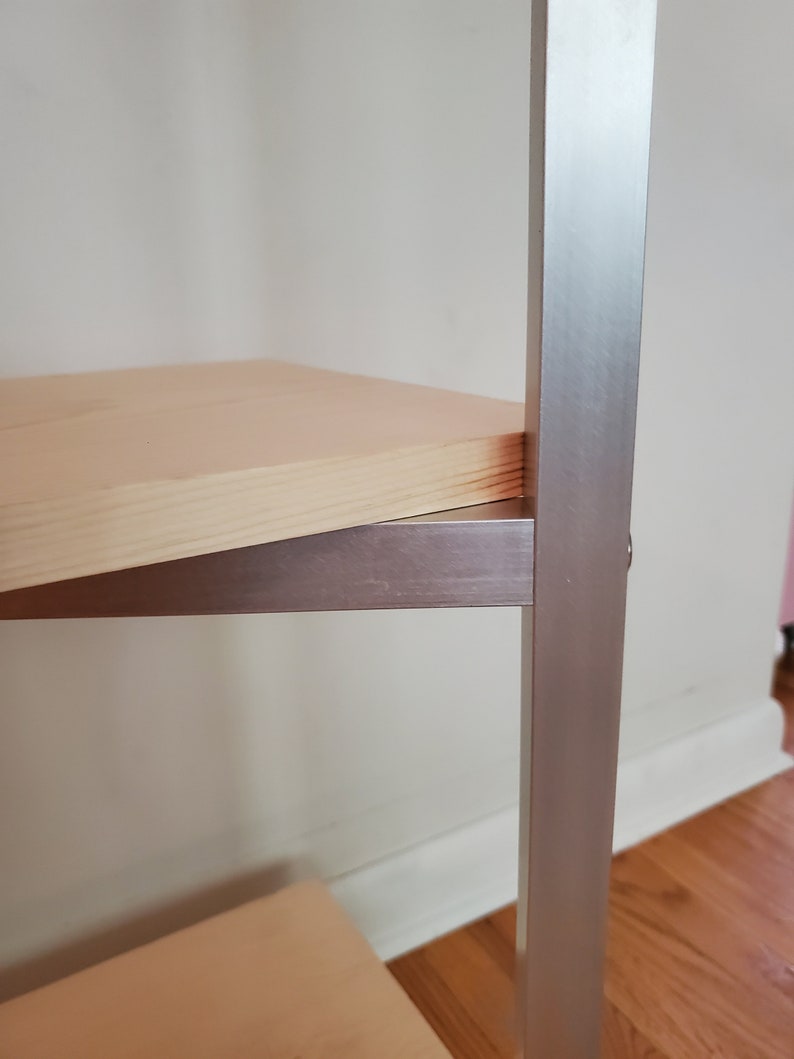 May include: A wooden shelf with a silver metal frame. The shelf is made of light wood and the frame is made of a brushed silver metal.