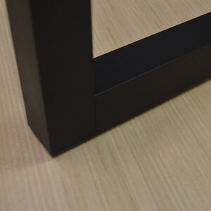 Puede incluir: Primer plano de una pata de mesa de madera negra con una superficie lisa y plana. La pata es de forma cuadrada y tiene un borde ligeramente redondeado.