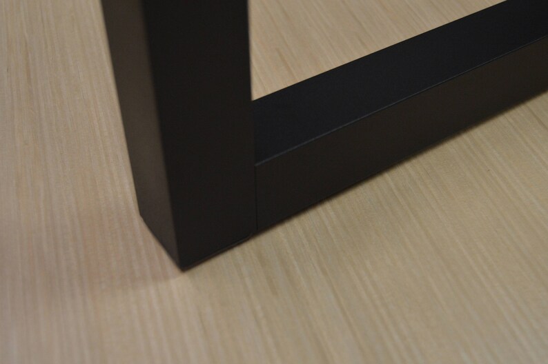 Puede incluir: Primer plano de una pata de mesa de madera negra con una superficie lisa y plana. La pata es de forma cuadrada y tiene un borde ligeramente redondeado.