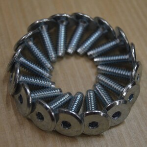 May include: A close-up of a circle of silver metal screws with flat heads and a hexagonal drive. The screws are arranged in a circle with the heads facing outwards.