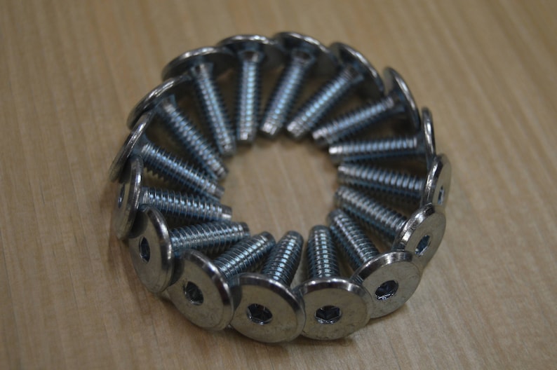 May include: A close-up of a circle of silver metal screws with flat heads and a hexagonal drive. The screws are arranged in a circle with the heads facing outwards.