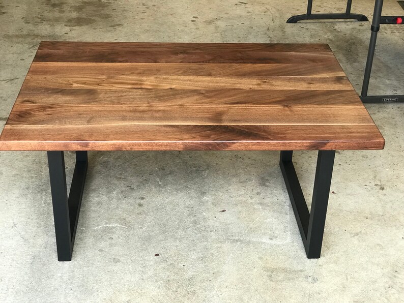 Puede incluir: Una mesa de centro rectangular con una tapa de madera oscura y patas de metal negro. La mesa tiene un dise&ntilde;o simple y moderno.