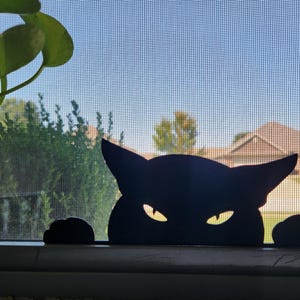 May include: A black cat silhouette with yellow eyes peeking over a windowsill. The cat's ears are pointed, and its paws are visible. The background shows a window screen, greenery, and a blue sky.