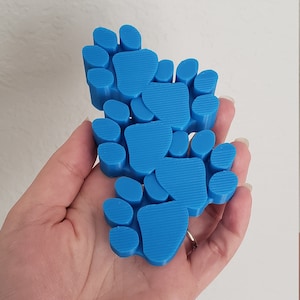 May include: A set of blue paw prints, made of plastic, arranged in a cluster. The paw prints are 3D printed and have a textured surface.