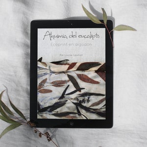 May include: A digital tablet displaying a book cover with the title "Alquimia del eucalipto" and the subtitle "Ecoprint en algodón" by Louise Upshall. The cover features a close-up of a fabric with a natural leaf print in shades of brown, green, and white.
