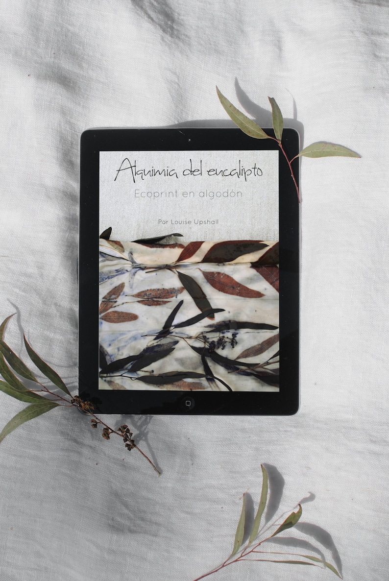 Może przedstawiać: Tablet cyfrowy wyświetlający okładkę książki z tytułem "Alquimia del eucalipto" i podtytułem "Ecoprint en algod&oacute;n" autorstwa Louise Upshall. Okładka przedstawia zbliżenie tkaniny z naturalnym nadrukiem liści w odcieniach brązu, zieleni i bieli.