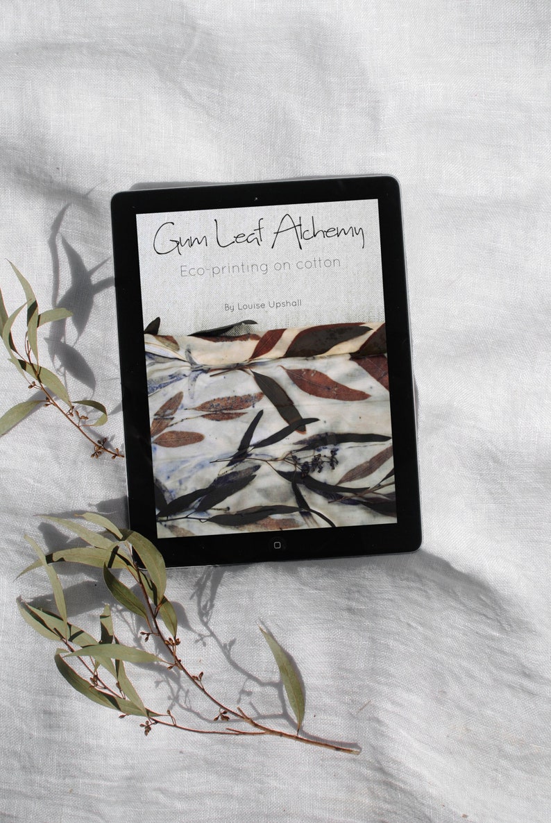 Peut inclure: Une tablette tactile affichant la couverture d'un livre intitul&eacute; "Gum Leaf Alchemy: Eco-printing on cotton" par Louise Upshall. La couverture pr&eacute;sente un gros plan d'un tissu avec un motif de feuilles naturelles dans des tons de brun, rouge et blanc.