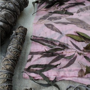 Peut inclure: Un tissu rose avec des motifs de feuilles brunes, un paquet de feuilles s&eacute;ch&eacute;es et un paquet de brindilles s&eacute;ch&eacute;es. Le tissu est pli&eacute; et a une couture le long du bord inf&eacute;rieur.