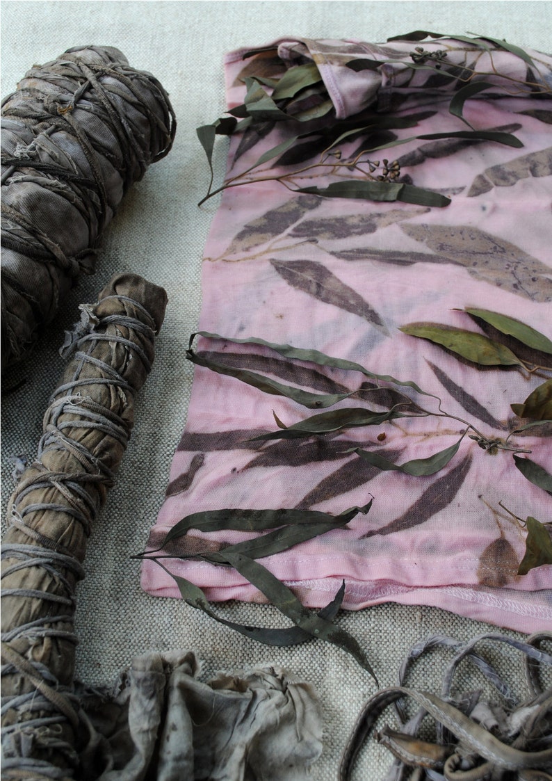 Peut inclure: Un tissu rose avec des motifs de feuilles brunes, un paquet de feuilles s&eacute;ch&eacute;es et un paquet de brindilles s&eacute;ch&eacute;es. Le tissu est pli&eacute; et a une couture le long du bord inf&eacute;rieur.