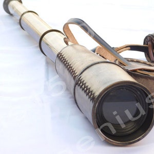 Puede incluir: Un telescopio de latón con una funda de transporte de cuero. El telescopio tiene un cuerpo de latón y una lente negra. La funda es de cuero marrón con costuras.
