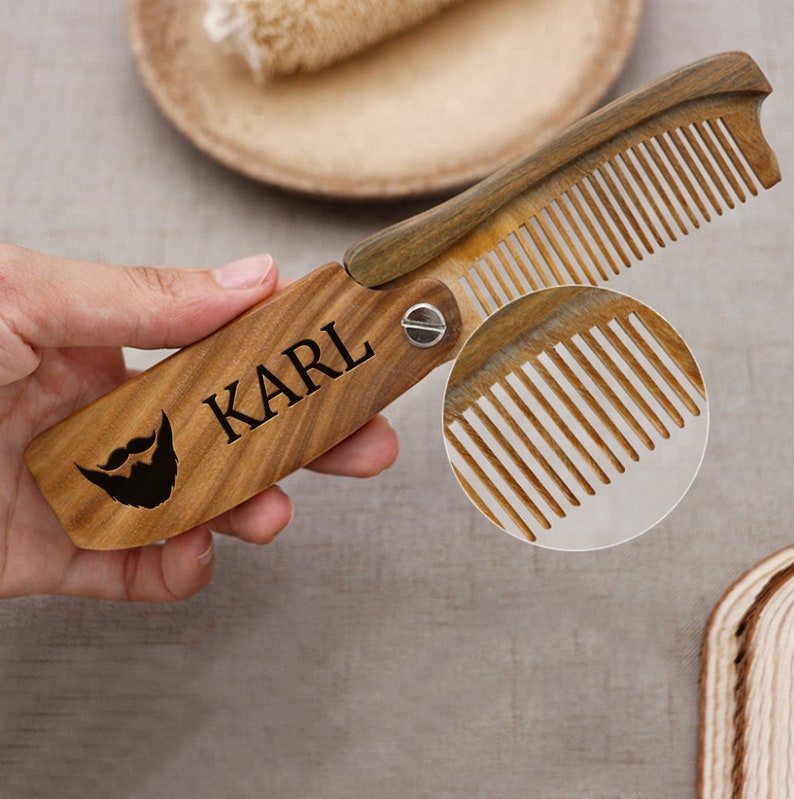 May include: A wooden comb with a beard icon and the name "KARL" engraved on it. The comb is folded in half and has a metal hinge.
