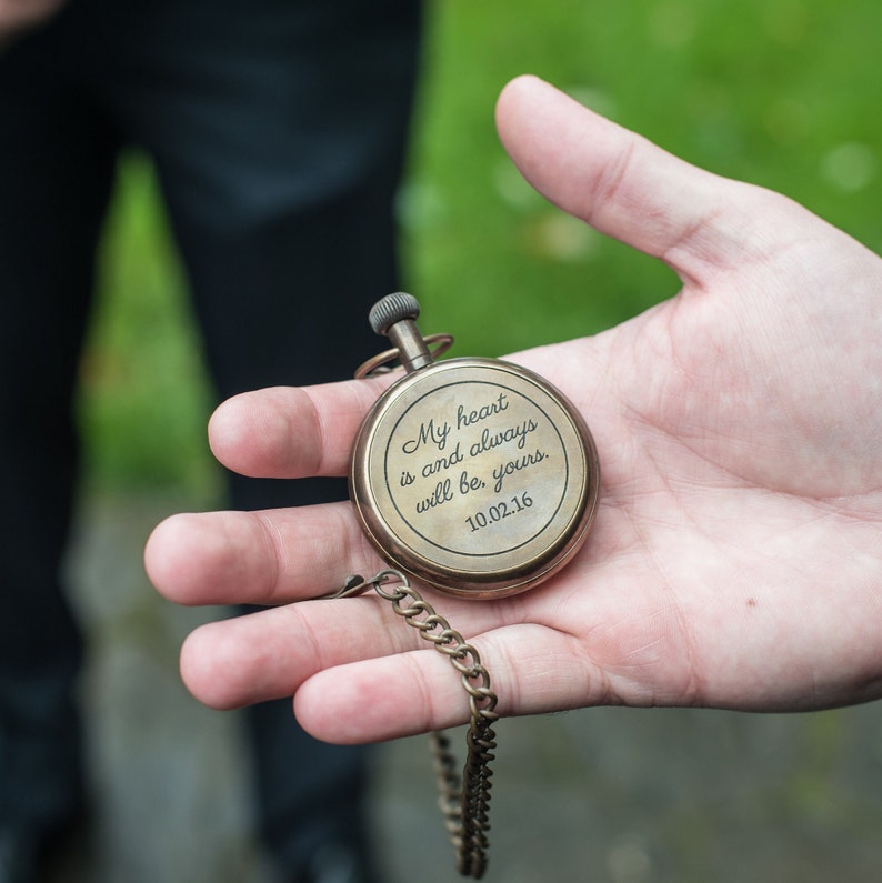 May include: A vintage brass pocket watch with a chain. The watch face has the inscription "My heart is and always will be, yours. 10.02.16". The watch is held in a person's hand.