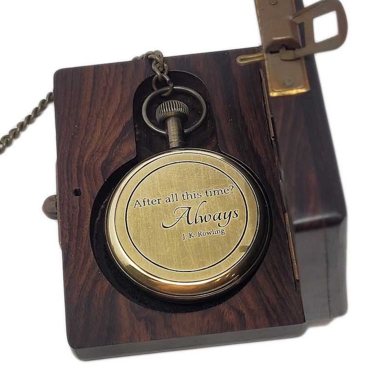 May include: A brass pocket watch, engraved with "After all this time? Always. J.K. Rowling", sits in an open dark wood box. The watch is connected to a chain. The box has a brass clasp and hinges.