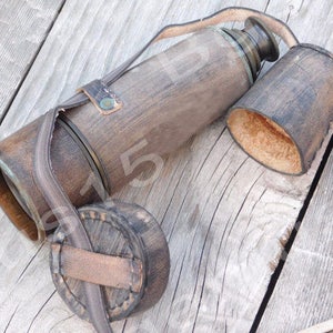 May include: A brown leather-wrapped flask with a brass lid and a matching leather carrying case. The flask has a wooden exterior and a brass cap.