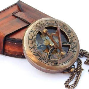 May include: A brass compass with a leather case and a chain. The compass has a sun dial and a directional compass. The compass is inscribed with "91, South Esplanade, E. London".