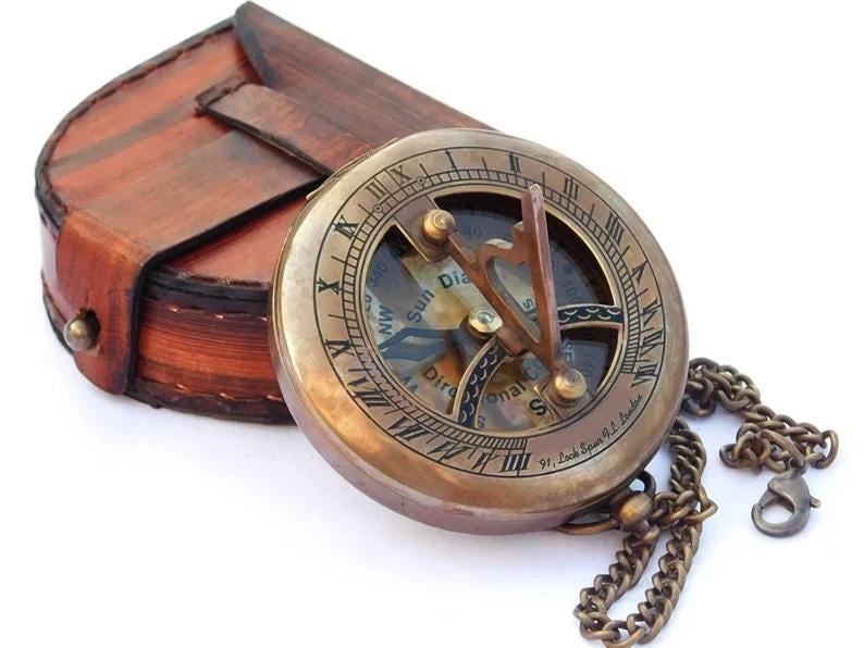 May include: A brass compass with a leather case and a chain. The compass has a sun dial and a directional compass. The compass is inscribed with "91, South Esplanade, E. London".