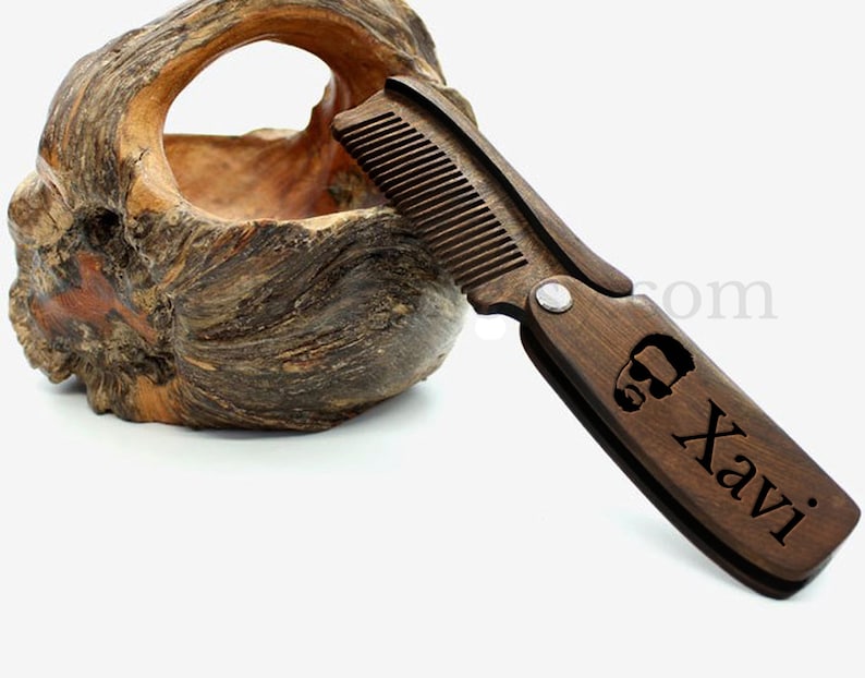 May include: A dark brown wooden comb with a folding design. The comb has a small metal hinge and is engraved with the name "Xavi" and a stylized image of a man's head.