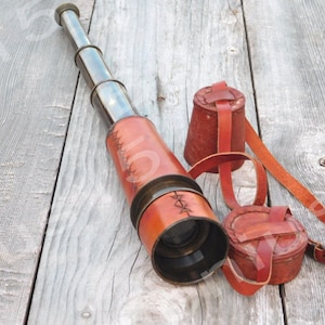 May include: A brass telescope with a leather covering and a brown leather carrying case. The telescope is lying on a wooden surface.