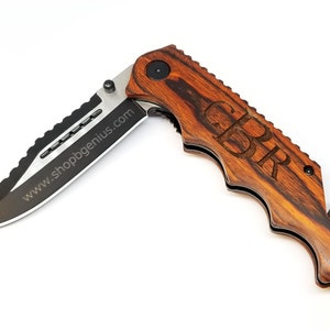 May include: A brown wooden folding pocket knife with a black blade and a safety feature. The knife has a personalized inscription that reads "GPR".
