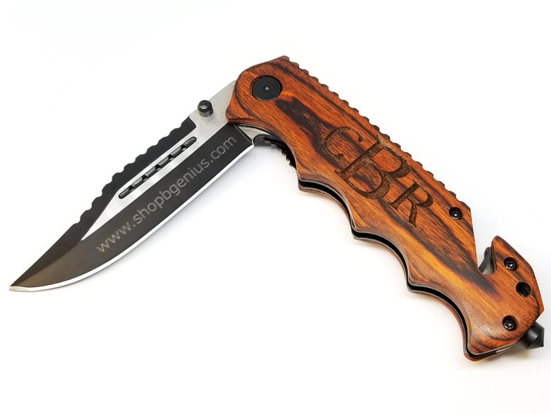 May include: A brown wooden folding pocket knife with a black blade and a safety feature. The knife has a personalized inscription that reads "GPR".
