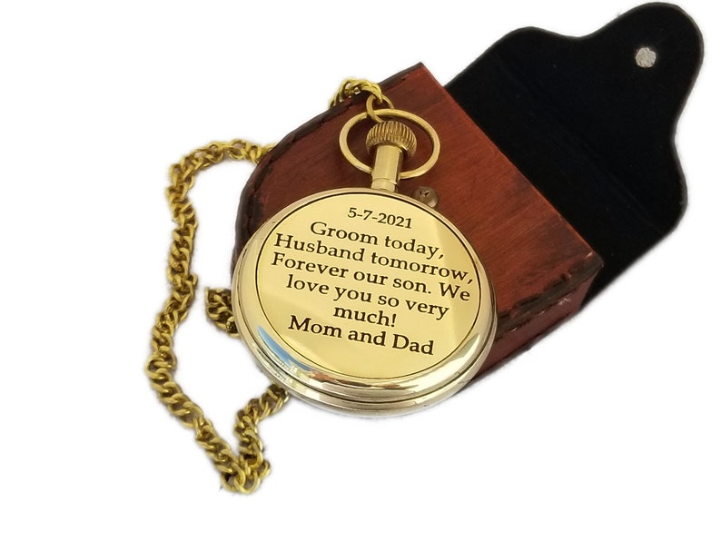 May include: A gold-coloured pocket watch with a chain, presented in a brown leather case. The watch face features engraved text: "Groom today, Husband tomorrow, Forever our son. We love you so very much! Mom and Dad."