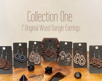 May include: Collection One: 7 Original Wood Dangle Earrings.  The earrings are displayed on black cards with gold glitter accents.  Each pair of earrings features a unique design, including a mandala, a mushroom, a star, and a teardrop.