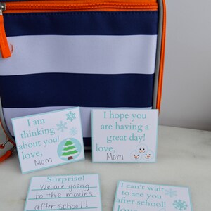 Op de afbeelding: Vier blauwe en witte kaartjes met handgeschreven berichten. De berichten luiden: "Ik denk aan je! Liefs, Mama", "Ik hoop dat je een fijne dag hebt! Liefs, Mama", "Verrassing! We gaan na school naar de bioscoop! Mama", en "Ik kan niet wachten om je na school te zien! Liefs, Mama".