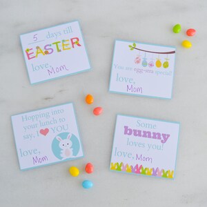 May include: Four colourful Easter-themed cards with messages such as "5 days till Easter" and "You are egg-stra special!" Each card has a blue background and is decorated with Easter-themed graphics. The cards are arranged on a white surface with colourful candy.