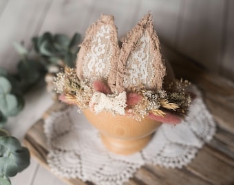 May include: A delicate headband with a pink and white bow, featuring a floral design with dried flowers and bunny ears made of lace and fabric.
