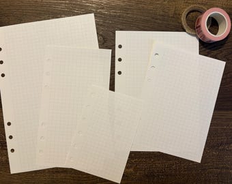 May include: Four white sheets of paper with a grid pattern and holes along the left edge. The sheets are arranged in a staggered pattern, with the largest sheet at the bottom and the smallest sheet at the top.