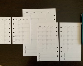 May include: White planner inserts with monthly calendar layouts, featuring boxes for each day and space for notes. The inserts have pre-punched holes for binding and include a teal pen.