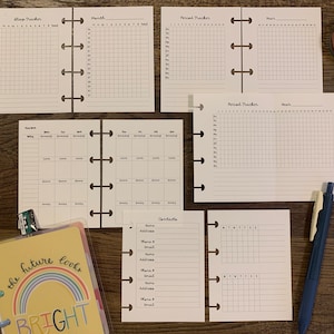 May include: A set of printable planner pages for a personal organizer. The pages include trackers for sleep, periods, monthly calendars, weekly calendars, contacts, and a yearly tracker. The pages are printed on white paper and have a grid pattern.