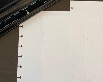 May include: A black Happy Planner punch with the text "The Happy Planner" and "Max 3 Sheets" on it. The punch is next to two white sheets of paper with holes punched along the left side.