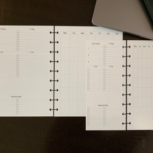 May include: A white planner with a black spiral binding. The planner has sections for "Top 3 Goals", "To Do", "To Blog", "Important Dates", and a weekly calendar.