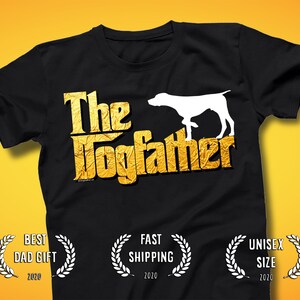 Puede incluir: Camiseta negra con el texto "The Dogfather" en letras doradas y una silueta de perro blanca. La camiseta también tiene el texto "Best Dad Gift 2020", "Fast Shipping 2020" y "Unisex Size 2020".
