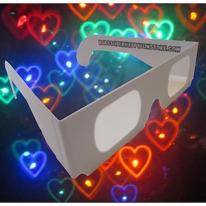 May include: White plastic 3D glasses with a website address printed on the side. The glasses are in front of a blurry background of colorful heart-shaped lights.