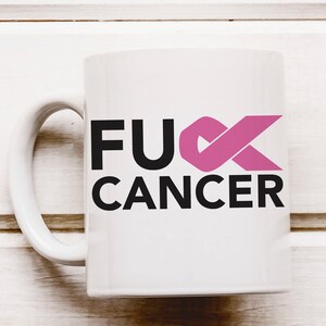 Op de afbeelding: Witte keramische koffiemok met een zwarte en roze afbeelding met de tekst "F**K CANCER" met een roze lint.