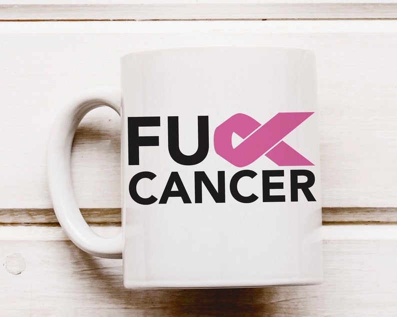 Op de afbeelding: Witte keramische koffiemok met een zwarte en roze afbeelding met de tekst "F**K CANCER" met een roze lint.