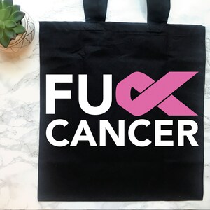 Op de afbeelding: Zwarte tote bag met witte tekst die "F**K CANCER" zegt en een roze lint.