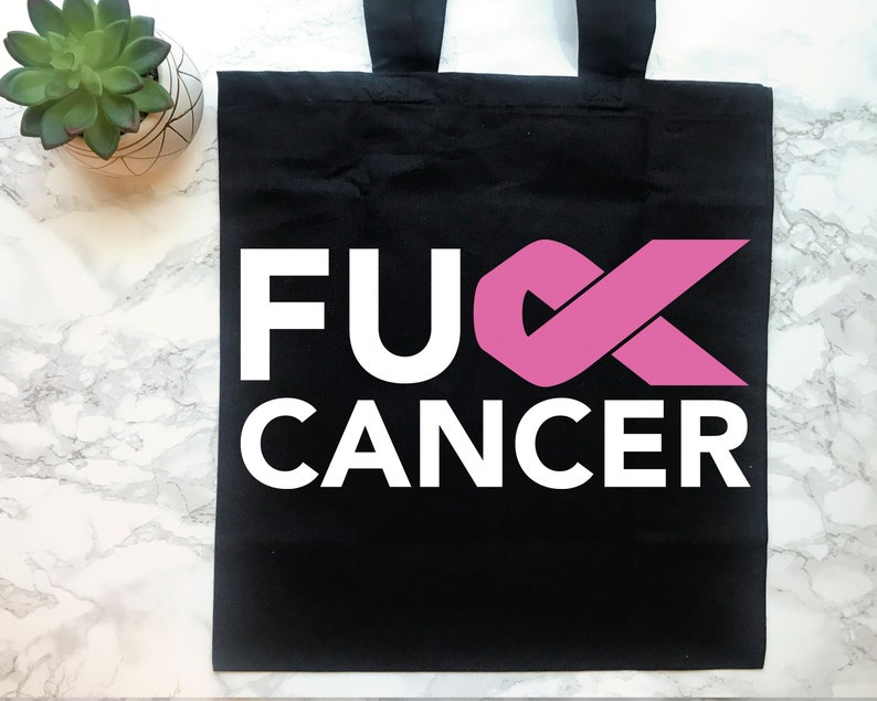 Op de afbeelding: Zwarte tote bag met witte tekst die "F**K CANCER" zegt en een roze lint.