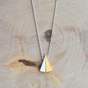 Puede incluir: Un collar de cadena de plata con un colgante hecho de dos triángulos, uno mitad dorado y el otro mitad blanco.