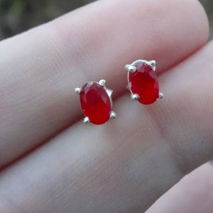 May include: A pair of silver stud earrings with oval-shaped red gemstones.