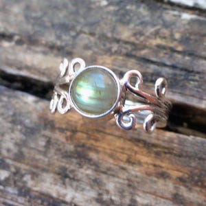 May include: A silver ring with a green and blue iridescent gemstone set in a delicate, swirling design.
