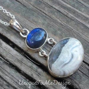 May include: A silver necklace with a pendant featuring two oval-shaped stones. The top stone is a dark blue labradorite, and the bottom stone is a white and gray agate.