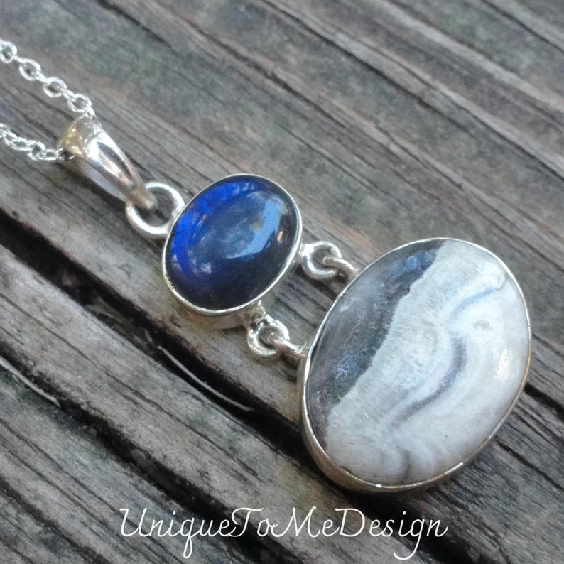 May include: A silver necklace with a pendant featuring two oval-shaped stones. The top stone is a dark blue labradorite, and the bottom stone is a white and gray agate.