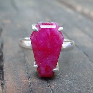 Pode incluir: Um anel de prata com uma grande gema rosa facetada em forma de caixão.