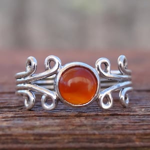 May include: A silver ring with an orange gemstone set in a delicate, swirling design.