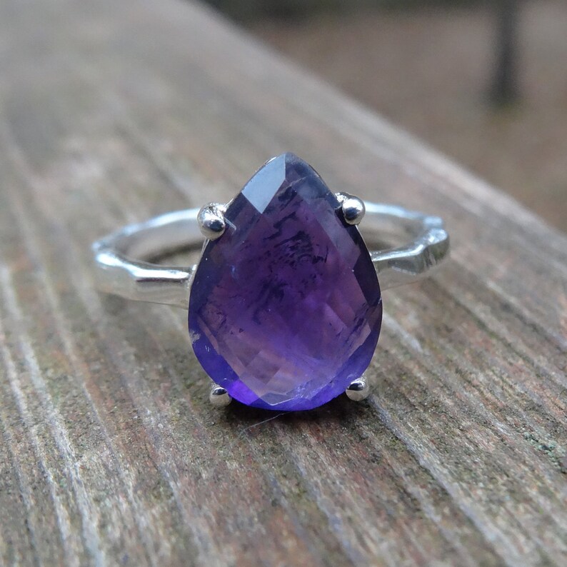 May include: A silver ring featuring a large, pear-shaped amethyst gemstone. The ring has a textured band.
