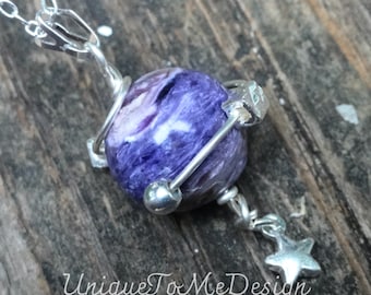 May include: A silver necklace with a purple and white gemstone pendant. The pendant is surrounded by silver wire and has a small silver star charm hanging from it. The necklace is on a wooden surface.
