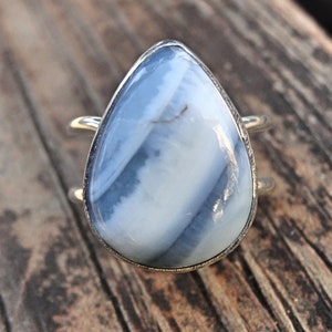 May include: A silver ring featuring a large, teardrop-shaped gemstone with a blue and white striped pattern. The ring has a double-band design, and the stone is set in a silver bezel.